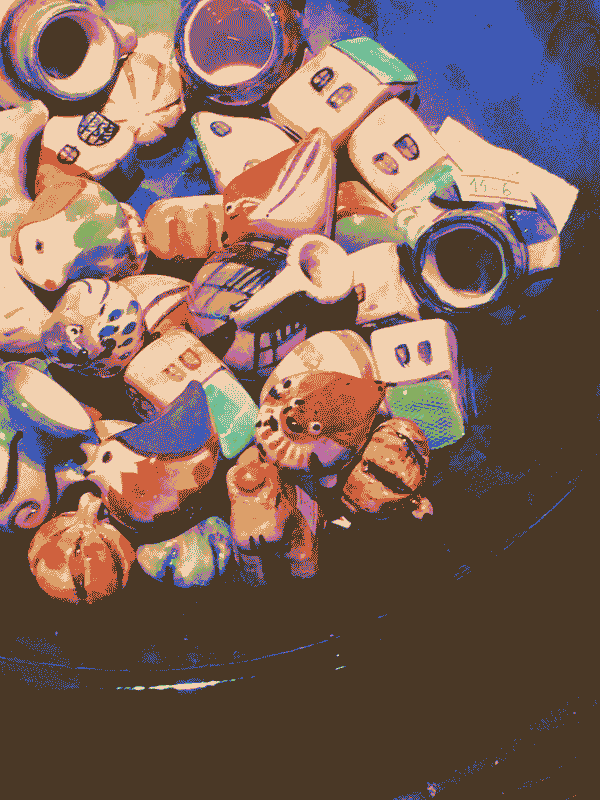 a bowl of colorful ceramics. in center frame, a cute red ceramic bird eyes the camera